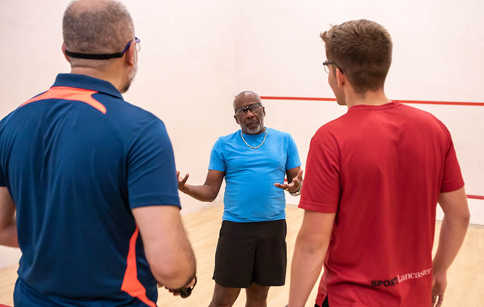 A coach instructing two squash players